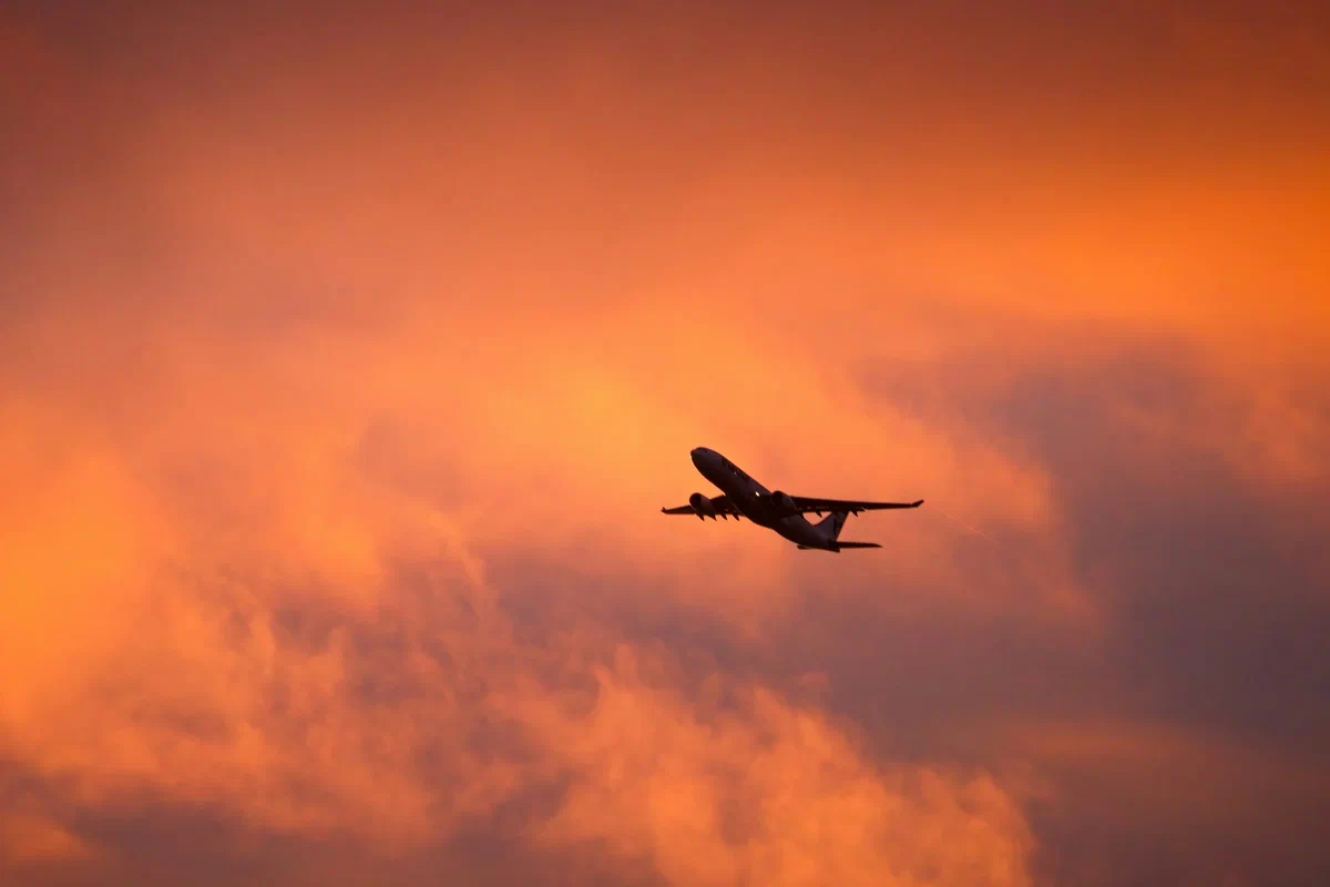 Avion de pasageri în urcare, în siluetă pe un cer portocaliu de apus